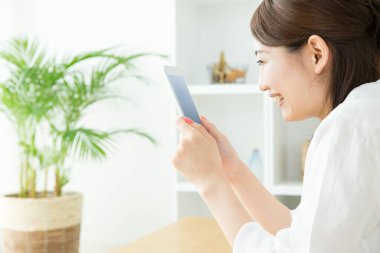 Genç Asyalı kadın oturma odasında tablet kullanıyor.