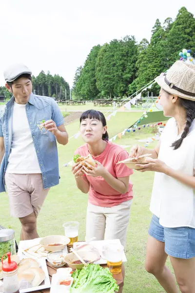happy Japanese friends enjoying barbecue at nature