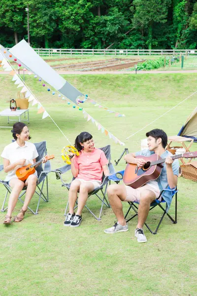 happy asian friends playing musical instruments in camping park