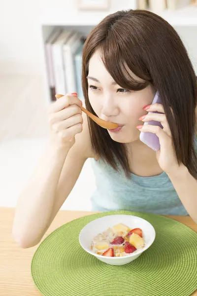 美丽的亚洲女人正在用智能手机与白人交谈 吃着健康的早餐 — 图库照片