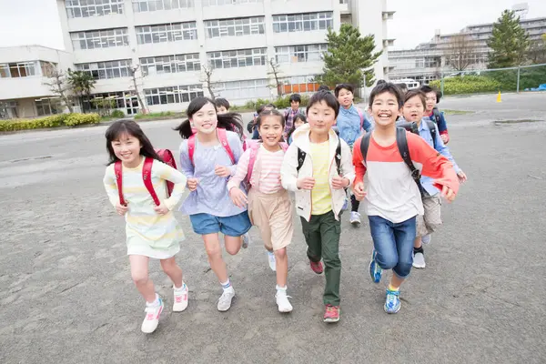 学校の庭で走っているバックパックを持つ日本の子供たちのグループ — ストック写真