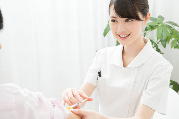 молодая медсестра обеспечивает инъекцию для азиатской женщины.