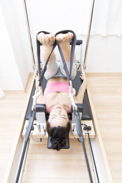 sporty Japanese woman in sportswear training with reformer indoors