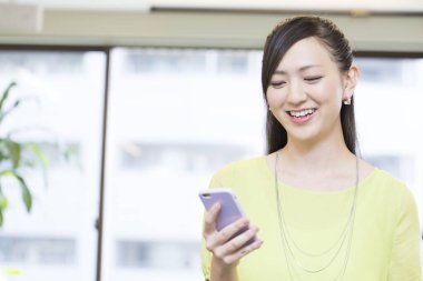 Genç Asyalı kadın ofiste akıllı telefon kullanıyor. 