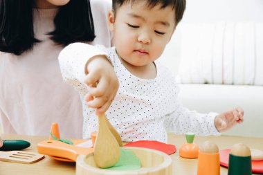 Asyalı anne ve oğlu evde tahta oyuncaklarla oynuyorlar. 