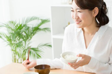 Asyalı kadın evde çubuklarla yemek yiyor.