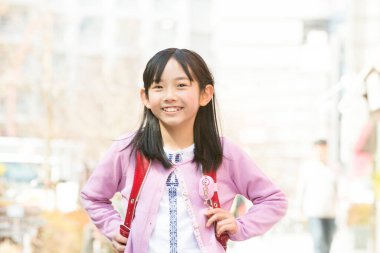 Genç Asyalı kız gülümsüyor ve şehirde kameraya bakıyor.