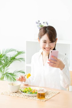 Kadın mutfakta yemek yerken cep telefonu kullanıyor.