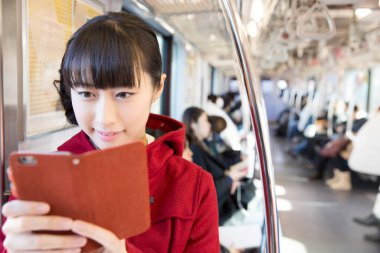 Trende akıllı telefon kullanan genç bir Japon kadın. 