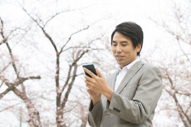 Parkta akıllı telefonu olan genç Asyalı iş adamı.