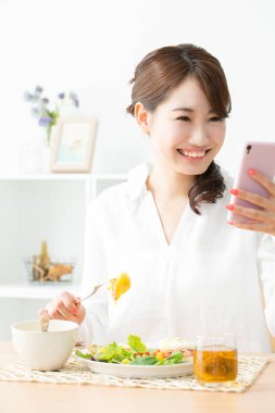 Kadın mutfakta yemek yerken cep telefonu kullanıyor.