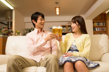Genç Asyalı çift oturma odasında bira içiyor.
