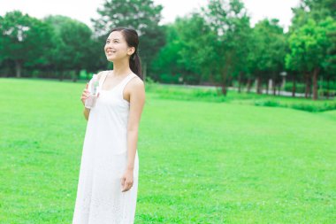 Yeşil yaz parkında gündüz vakti su içen güzel Japon kadın. 