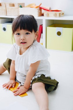 Küçük tatlı Japon kız oturma odasında oyuncaklarla oynuyor.