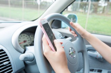 Araba kullanırken elinde akıllı telefon tutan kadın.