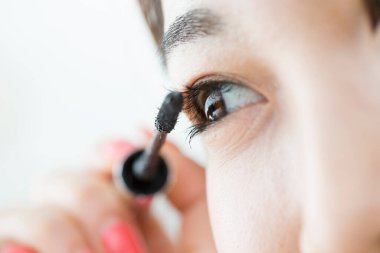 Bir kadın evde kirpiklerine rimel sürüyor. 