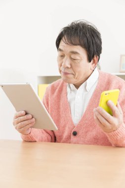 Oturma odasında tablet bilgisayarı ve akıllı telefonu olan son sınıf öğrencisi.