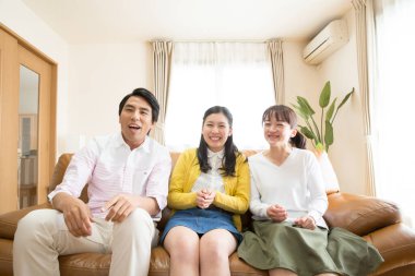  Asyalı bir aile kanepede oturmuş televizyon seyrediyor. 