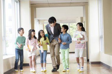 Öğretmenli bir grup Japon çocuk okul koridorunda yürüyor. 