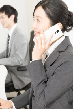 Bilgisayarla çalışan genç adam ve telefonda konuşan iş arkadaşı kadın. 