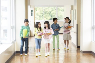 Okul koridorunda yürüyen kitaplarla bir grup Japon çocuk. 