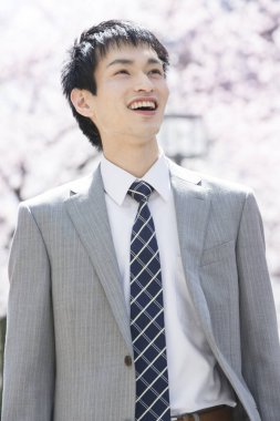 Genç Japon iş adamının çiçek açan sakura arka planındaki yakın plan portresi.