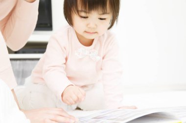 Genç Asyalı anne ve tatlı kız evde kitap okuyorlar.