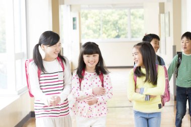 Okul koridorunda sırt çantalı bir grup Japon çocuk yürüyor. 