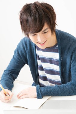 Masada deftere yazı yazan genç Asyalı adam. 