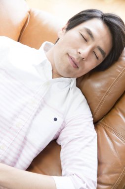 Genç Asyalı adam evdeki kanepede dinleniyor..