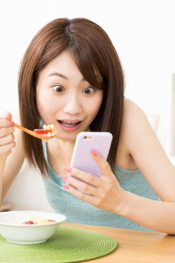 Akıllı telefon beyazı kullanan güzel Asyalı kadın sağlıklı kahvaltı yapıyor.