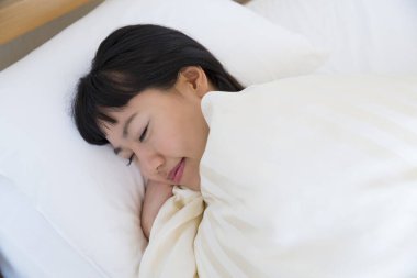 Beyaz yatakta uyuyan Asyalı kadın.