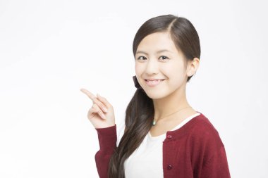 Genç Asyalı kadın beyaz arka planda bir şeye işaret ediyor.