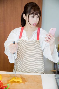 Asyalı kadın şef mutfakta akıllı telefon kullanıyor.