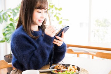 Japon restoranında yemek yerken akıllı telefon kullanan güzel genç bir kadın. 