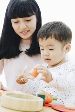 Asyalı anne ve oğlu evde tahta oyuncaklarla oynuyorlar. 