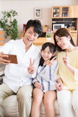 Üç kişilik Asyalı bir aile evdeki odada akıllı telefonuyla selfie çekiyor. 