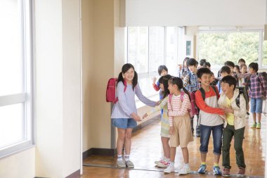 Okul koridorunda sırt çantalı bir grup Japon çocuk yürüyor. 