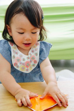 Güzel Asyalı bebek renkli kağıtlarla oynuyor.