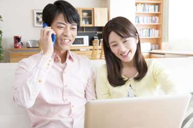 Genç adam evde bir kadınla dizüstü bilgisayar kullanırken akıllı bir telefon kullanıyor.