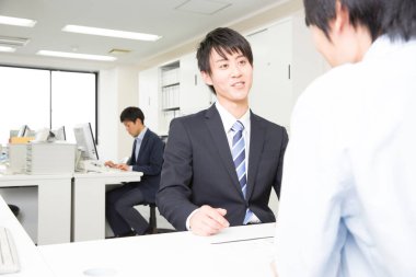 Genç Asyalı işadamı ofiste müşteriyle birlikte çalışıyor.