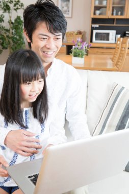 Evde dizüstü bilgisayar kullanan mutlu bir Asyalı aile.