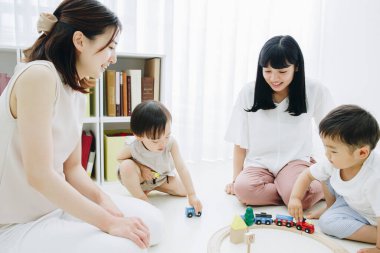 Neşeli Asyalı anneler ve çocuklar oturma odasında oynuyor.