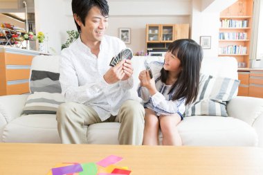 Baba ve kızı kanepede kağıt oynuyorlar.