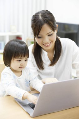 Genç anne ve küçük kızı evde dizüstü bilgisayar kullanıyorlar.