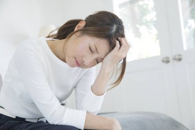 Asyalı kadın baş ağrısı çekiyor ve elini başının üstünde tutuyor.
