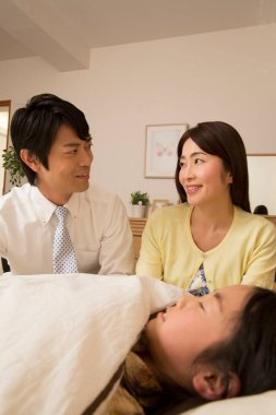 Kızı yatakta olan Asyalı bir aile.