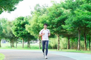 Genç yakışıklı Asyalı adam parkta koşuyor. 