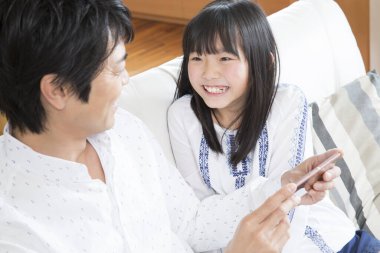 Gülümseyen baba ve kızı evde akıllı telefon kullanıyor.