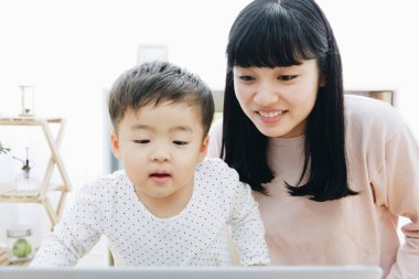 Asyalı anne ve oğlu dizüstü bilgisayarlarını birlikte kullanıyorlar.